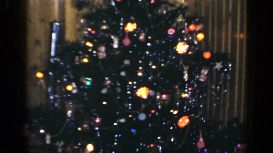 Lit Christmas tree with ornaments and tinsel inside a 1965 Long Island wood-paneled home interior.
