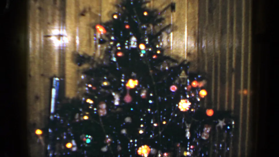1965 Long Island home-movie frame showing a lit Christmas tree with ornaments in a wood-paneled private interior.