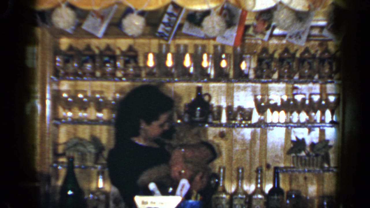 Woman behind a wooden bar hugs a small dog in a warmly lit shop interior.