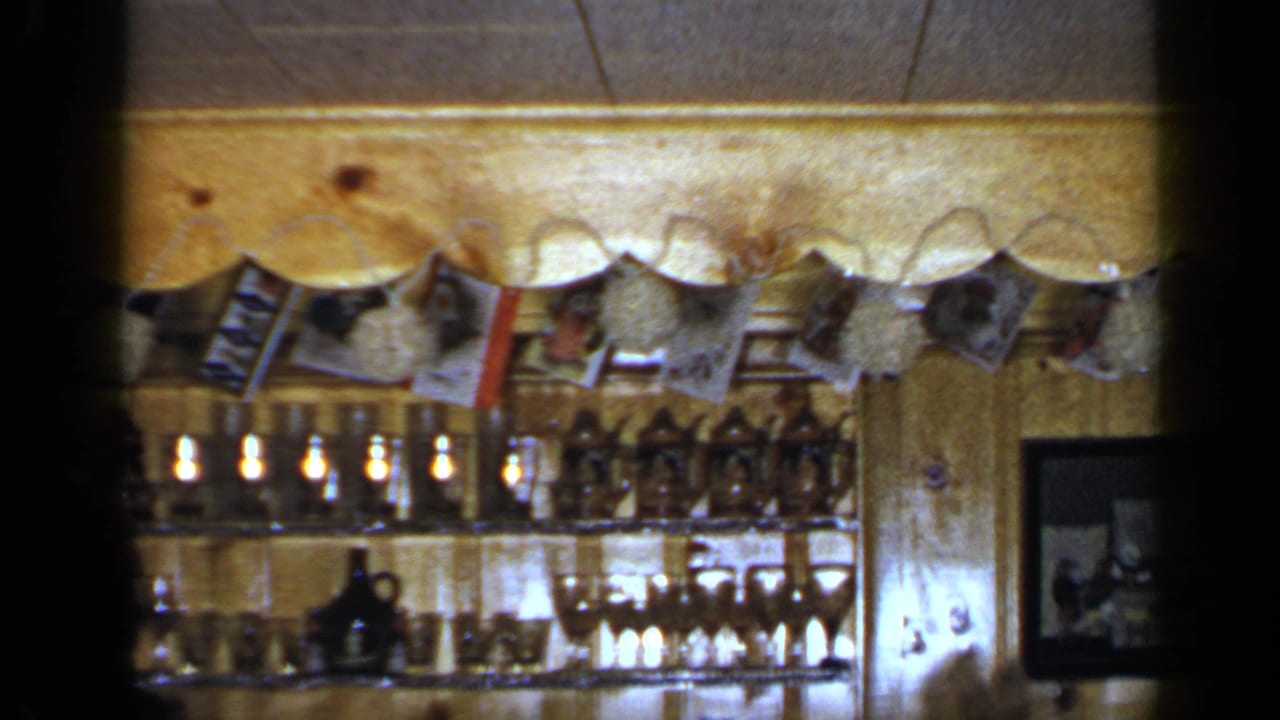 Wood-paneled room with shelves of glassware, hanging photos, and a framed group picture.