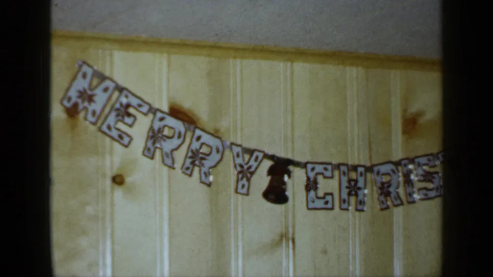 1965 Long Island frame with patterned Merry Christmas letters and a small bell shape against pale wood paneling.
