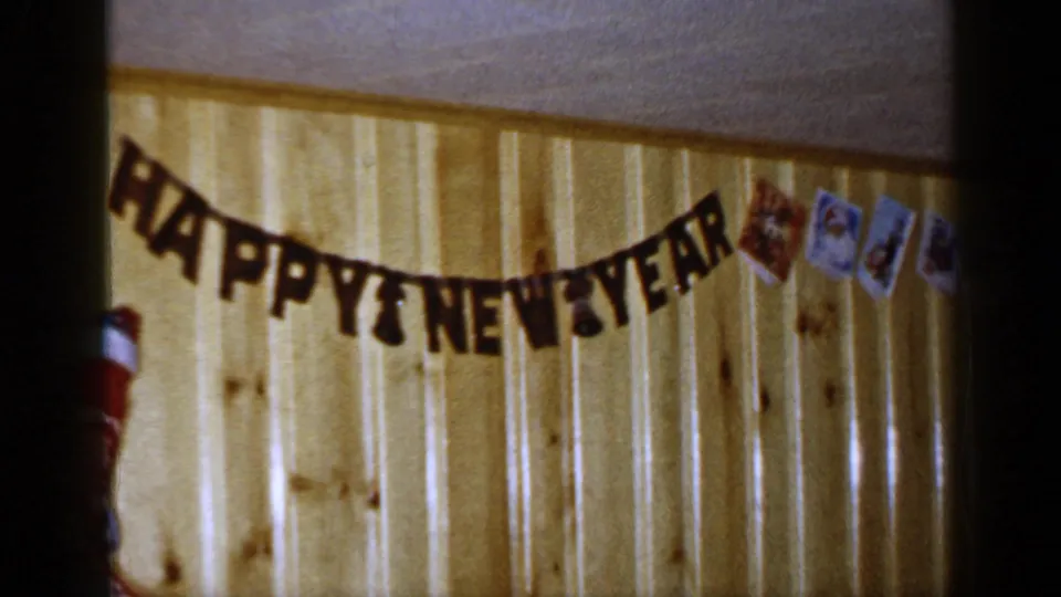 1965 Long Island interior frame showing the New Year banner across wood paneling, with a stocking edge and small holiday cards visible.