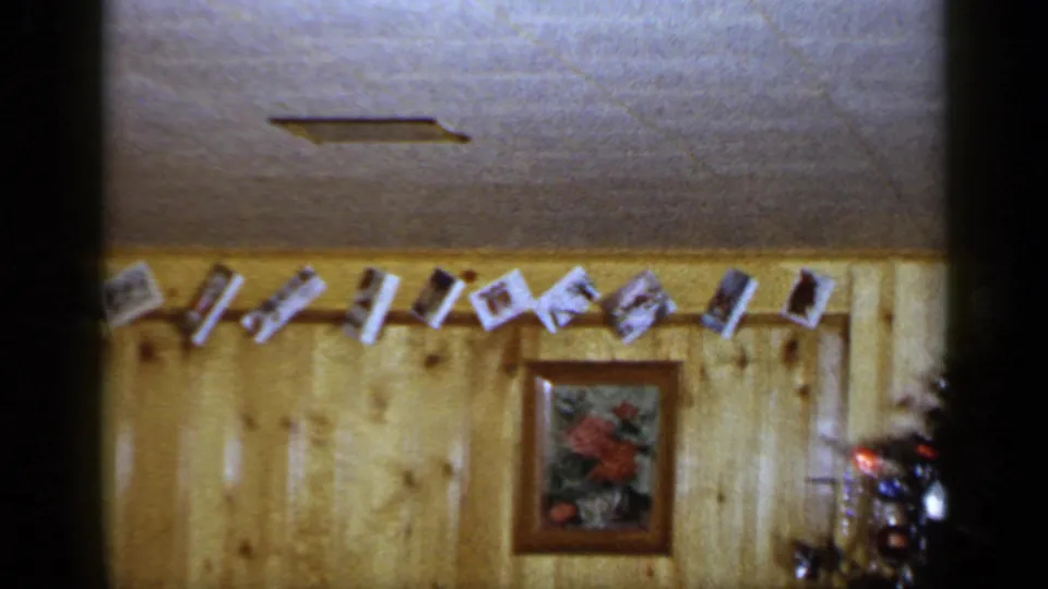 1965 Long Island holiday interior showing hanging cards, a framed floral picture, and the edge of a decorated Christmas tree.