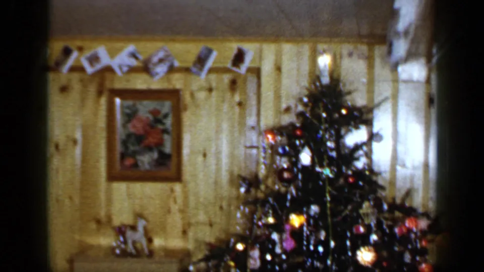 1965 Long Island holiday interior with a decorated Christmas tree, ornaments, lights, wall photo garland, and framed floral picture.