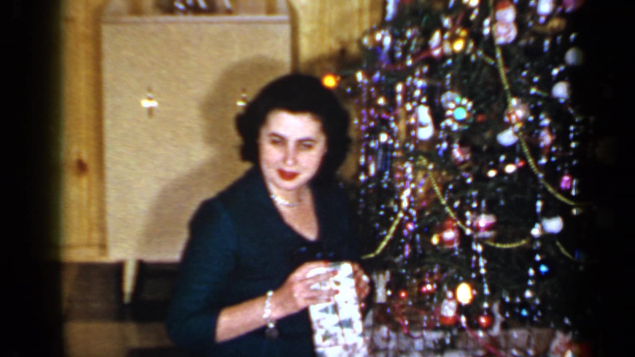 Woman seated beside a decorated Christmas tree holding a wrapped gift.