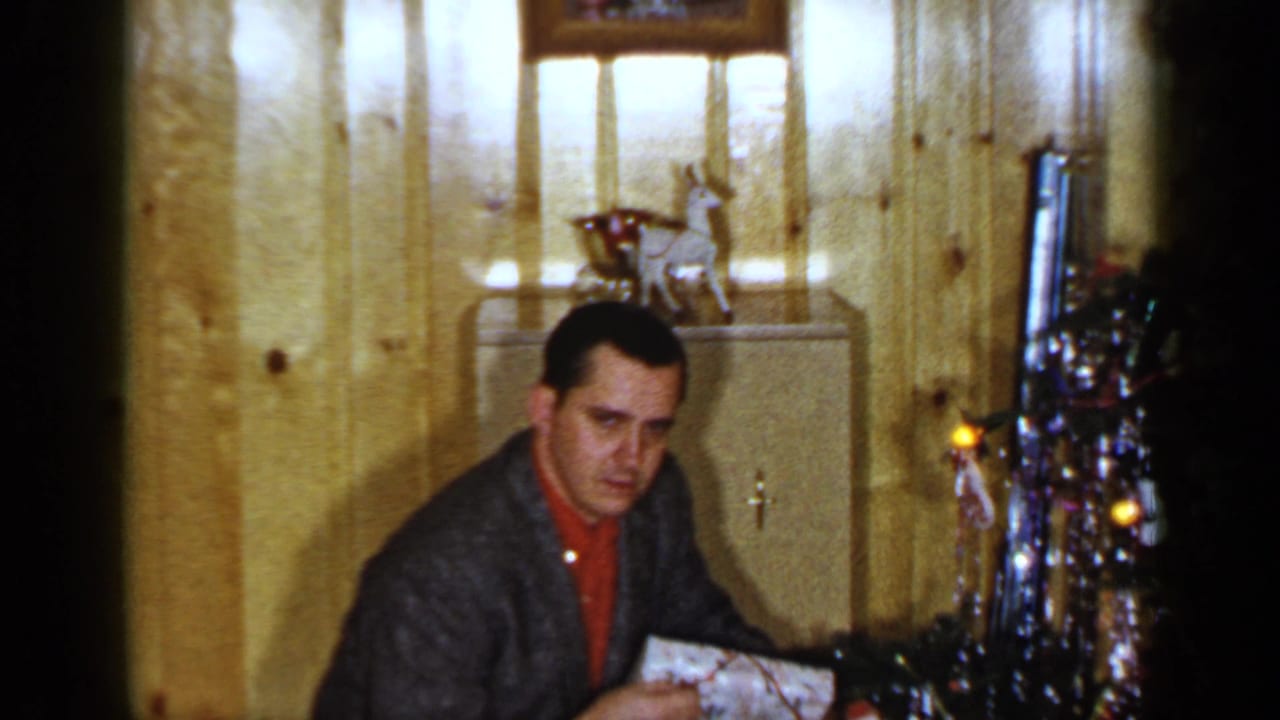 Man kneeling beside a decorated Christmas tree while holding a wrapped gift.