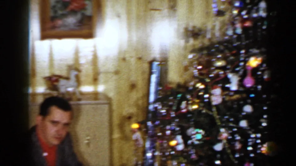 The final frame shows the man lower in the home-movie frame, with the decorated Christmas tree and curtained windows prominent.