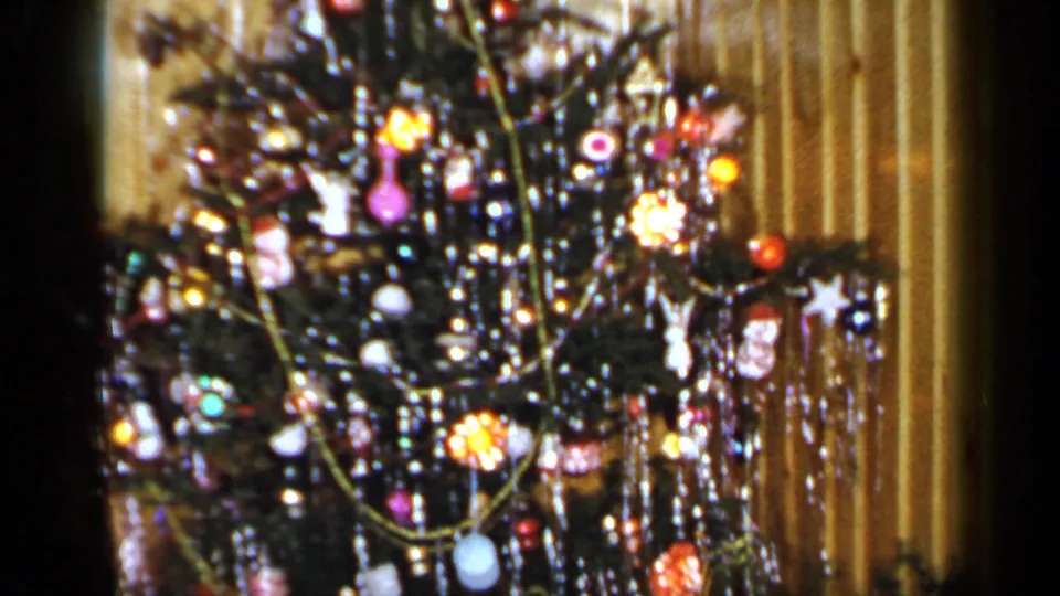 Close 1965 Long Island interior view of the holiday tree, showing dense tinsel, glass ornaments and warm lights against wood paneling.