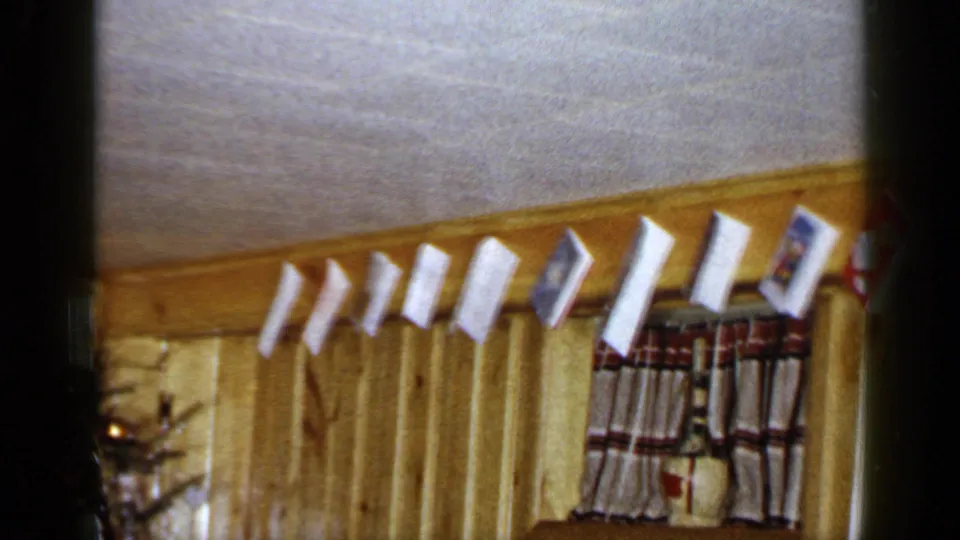Hanging Christmas cards line the upper wall of a wood-paneled Long Island home interior, with a curtain below.