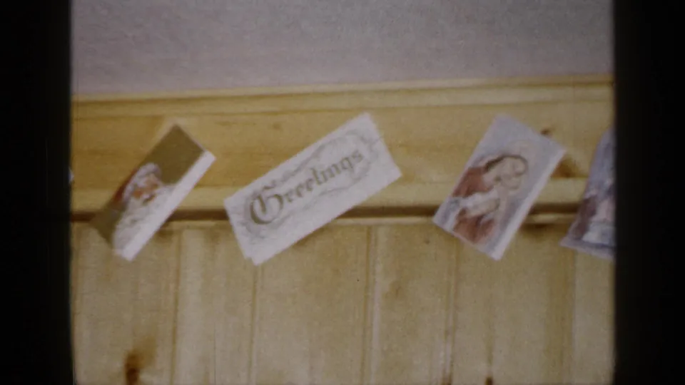A clipped card reading Christmas appears among religious cards on a wooden wall in the 1965 Long Island footage.