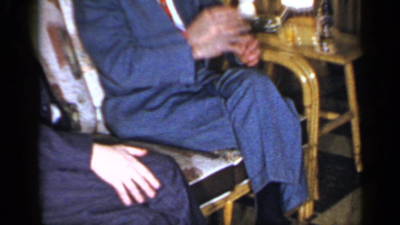 Cropped view of a seated adult in a blue suit holding a drink beside wicker furniture.