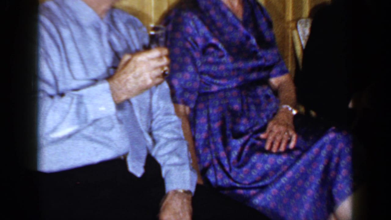 Partial view of the seated couple, showing the man's glass and the woman's patterned dress.