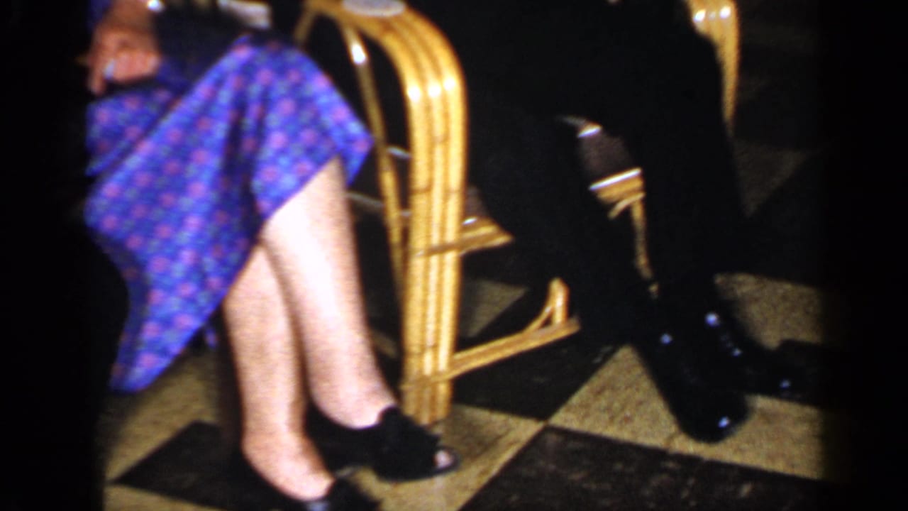 Seated adults in wicker chairs, including a woman in a blue patterned dress on a checkered floor.