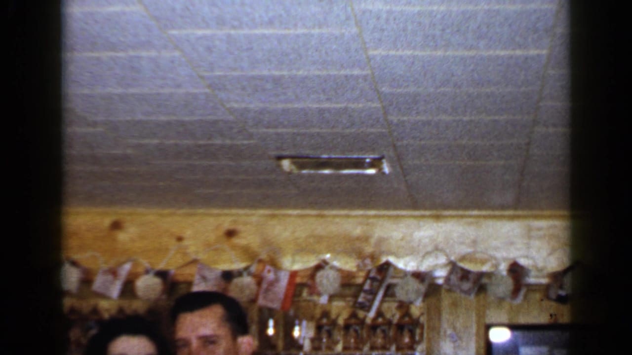 A couple is cropped low in frame inside a bar with garland and glassware.