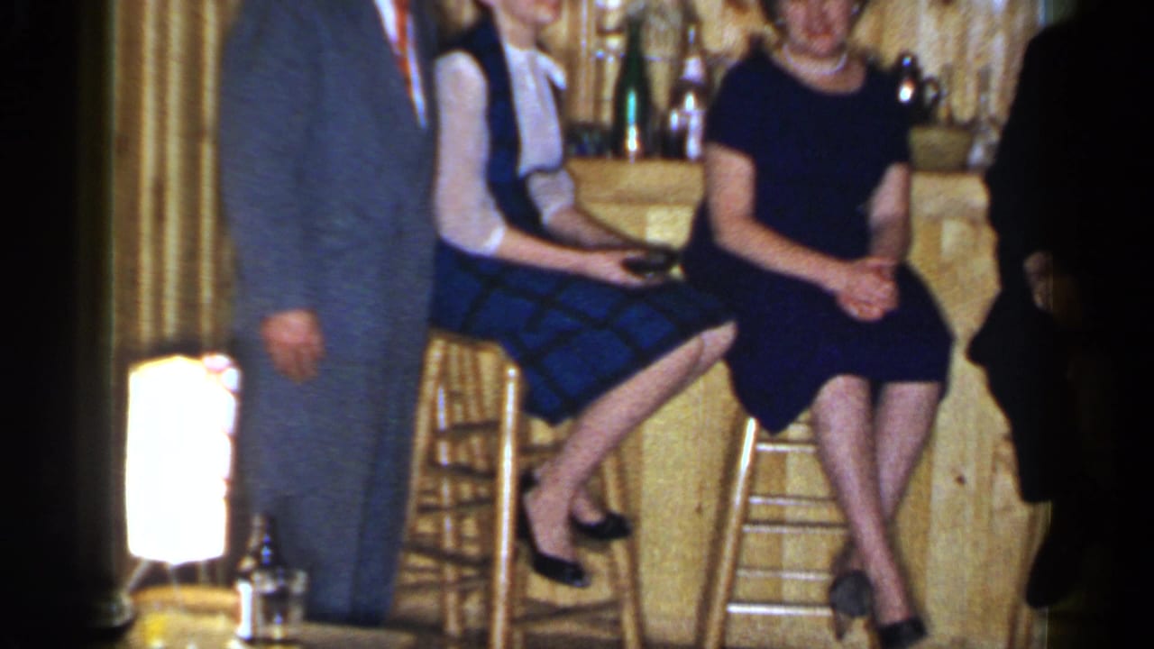 Two women sit on bar stools while a man stands partly cropped beside them.
