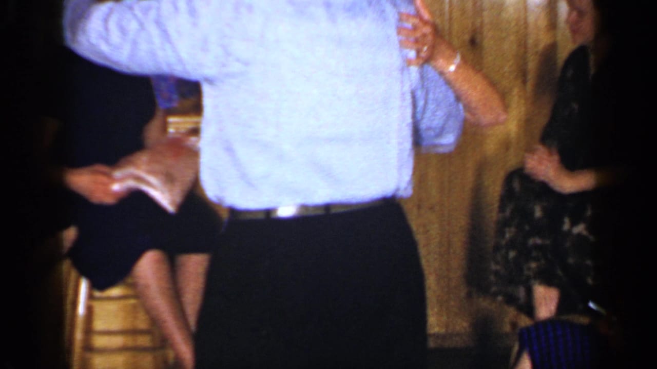 A dancing couple seen from behind with guests seated along the wall.