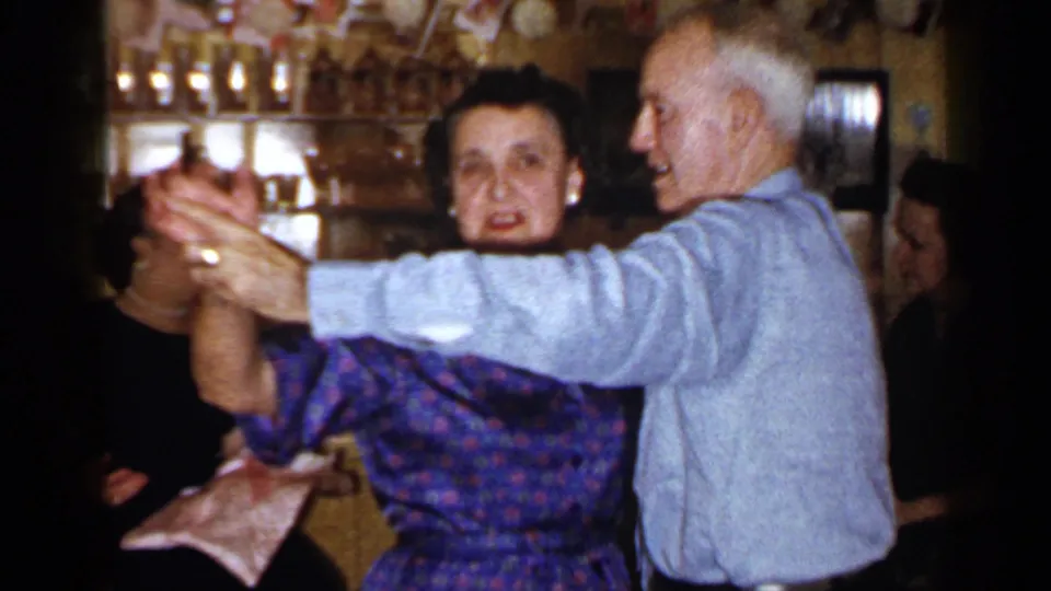 1965 Long Island 8mm frame showing an elderly couple dancing together in a crowded indoor family gathering.