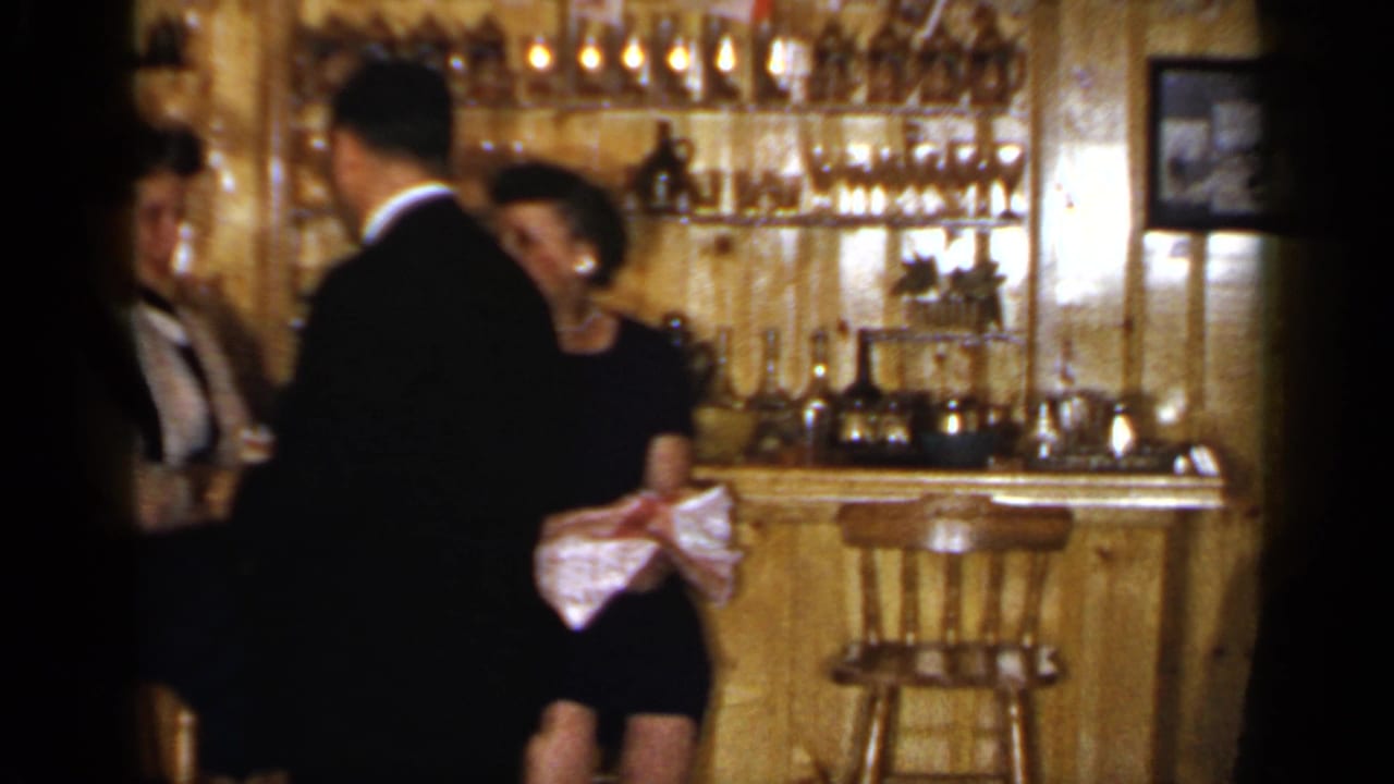 Adults gathered by a wood bar with glass shelves and bottles behind them.