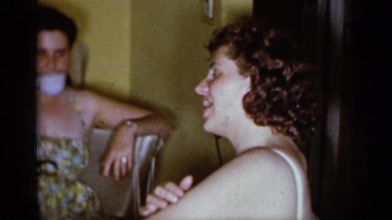 A smiling woman in a swimsuit faces another woman reflected in a mirror.