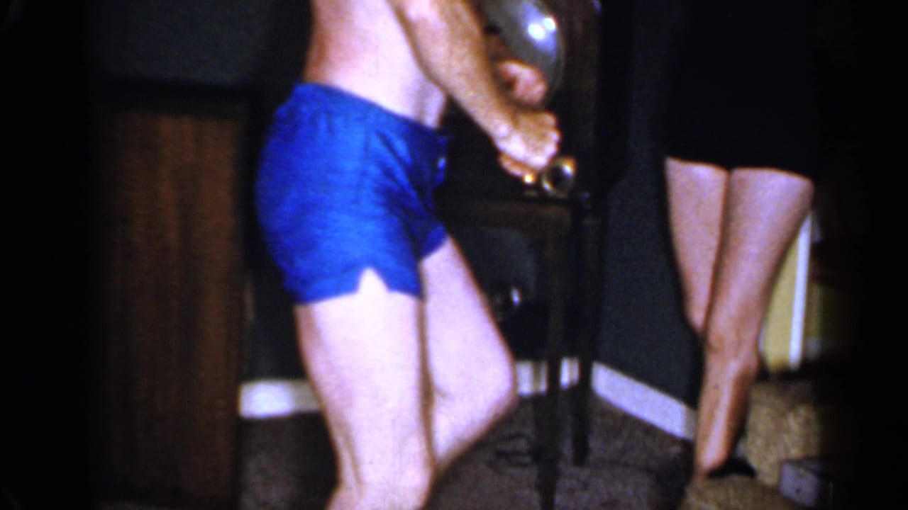 Barefoot man in blue trunks leans while a woman stands nearby.