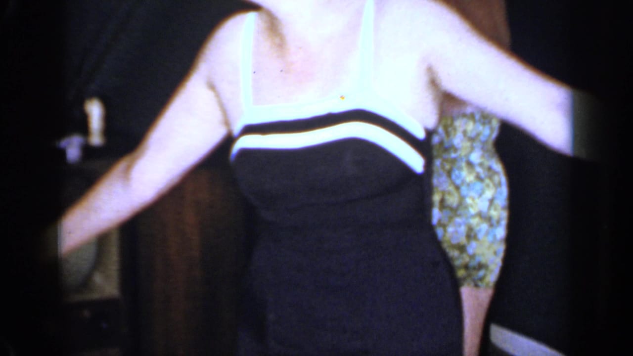 A woman in a black dress with white trim moves in a private Mineola room, with another patterned dress partly visible.
