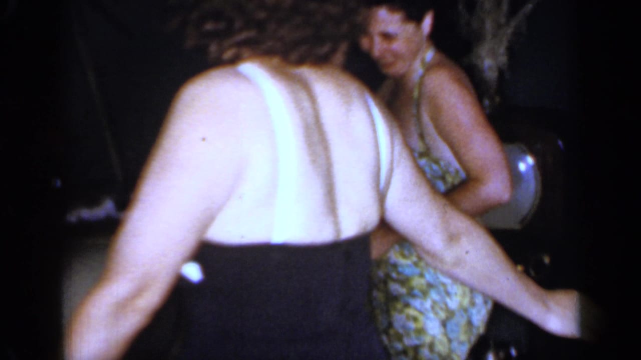 Two women in swimsuits move and talk in a dark outdoor setting.
