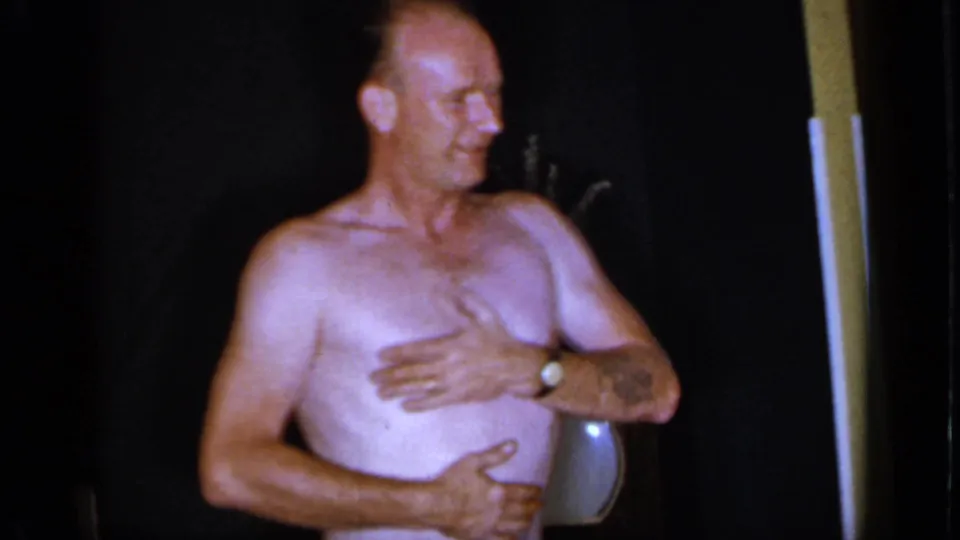 1966 Mineola home-movie frame showing a shirtless man near a doorway or post during a casual summer scene.