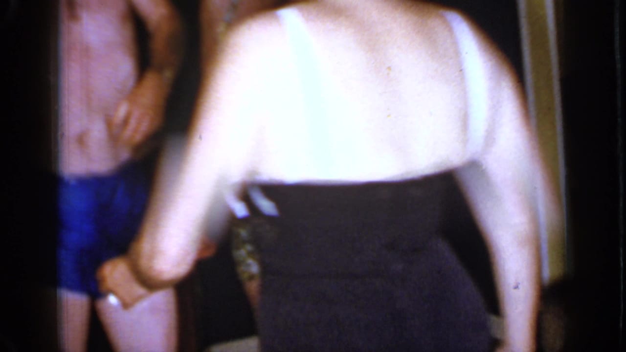 Woman in a black-and-white swimsuit passes close to the camera near adults in swimwear.