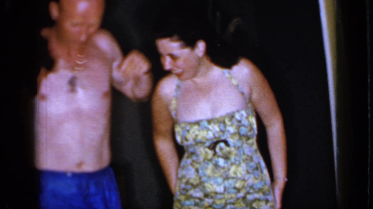 Shirtless man in blue trunks stands beside a woman in a floral bathing suit.
