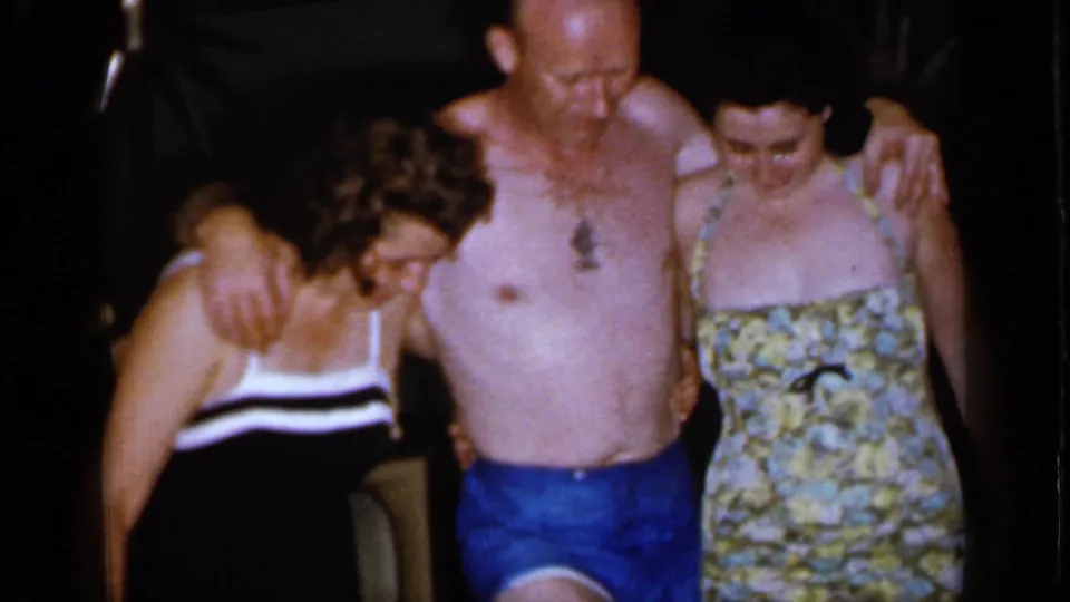 The 1966 Mineola home movie ends on three adults in swimwear leaning together, the man in blue trunks between two women as they look downward.