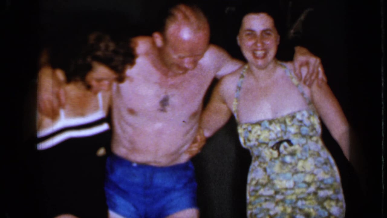 Three adults in swimsuits stand with arms linked and smile toward the camera.