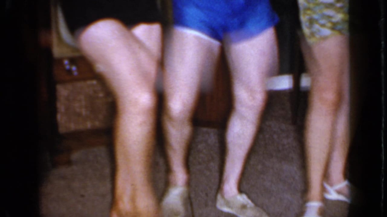 Lower-body view of adults in swimwear and sandals moving indoors in the 1966 Mineola home-movie clip.
