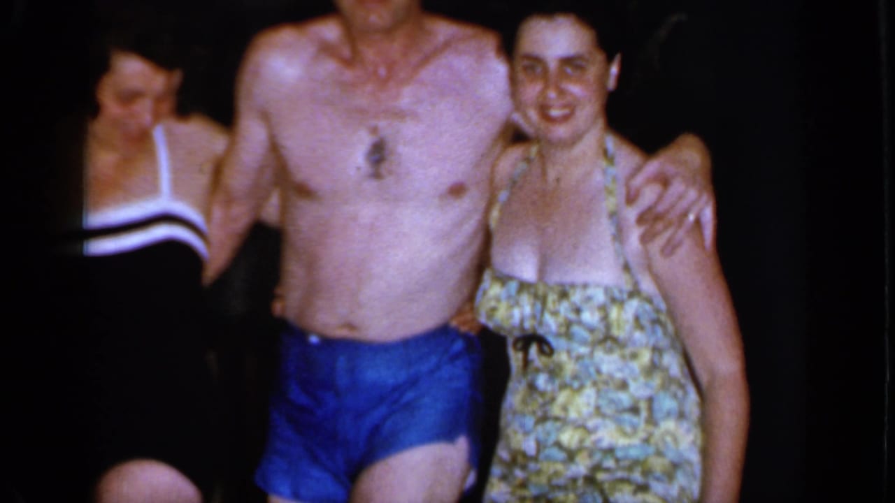 A smiling woman in a floral swimsuit stands close to a shirtless man in blue trunks, with another woman partly visible in the 1966 Mineola scene.
