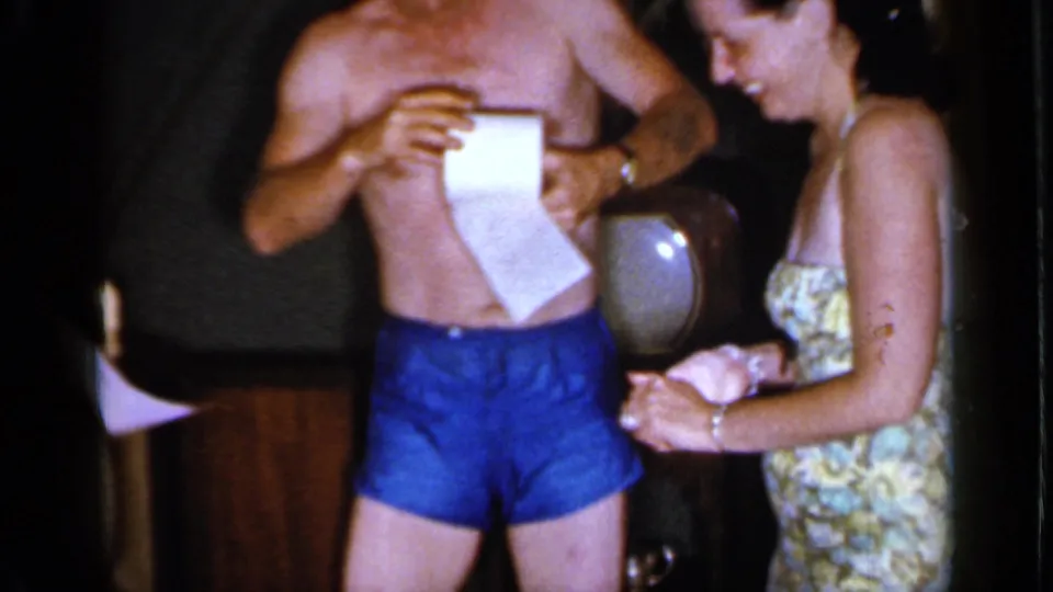 At the 1966 Mineola gathering, the man unwinds toilet paper while a woman in a patterned dress stands beside him.
