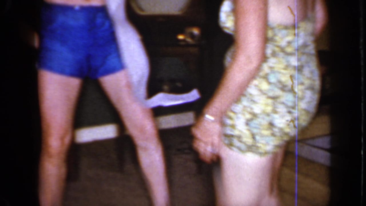 Cropped view of adults in swimwear standing in a dark home interior.