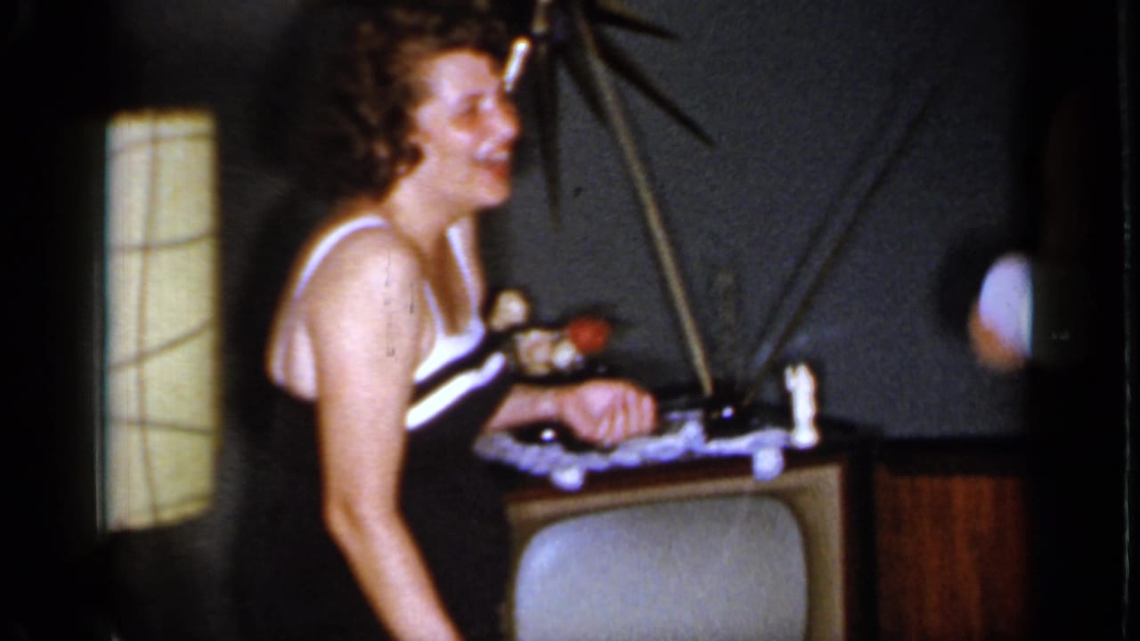 Woman in black and white swimsuit laughing beside a table and television antennae.