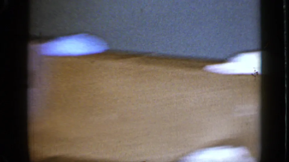 The final frame is an unfocused 8mm view of a tan surface and small white objects, likely captured during a quick handheld movement indoors.
