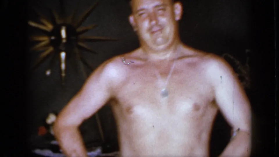 A smiling shirtless adult man moves closer to the handheld camera in the 1966 Mineola interior footage.