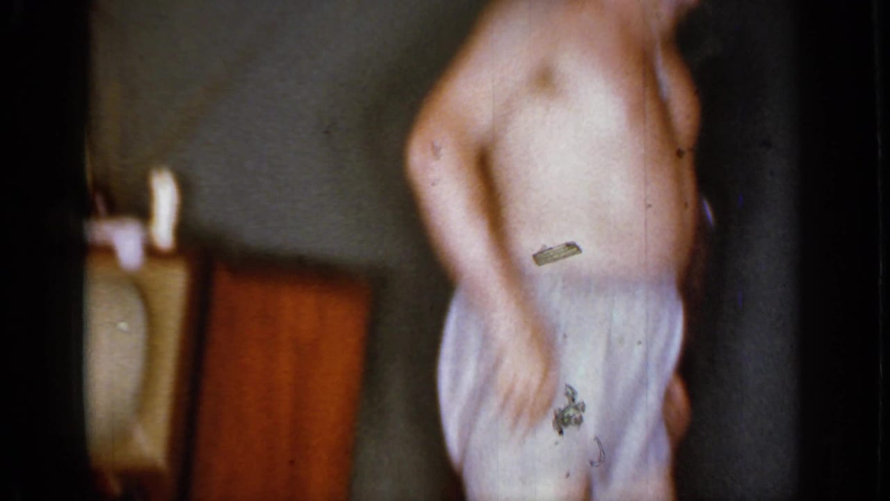 Shirtless man in light boxers dancing in a dim indoor room.