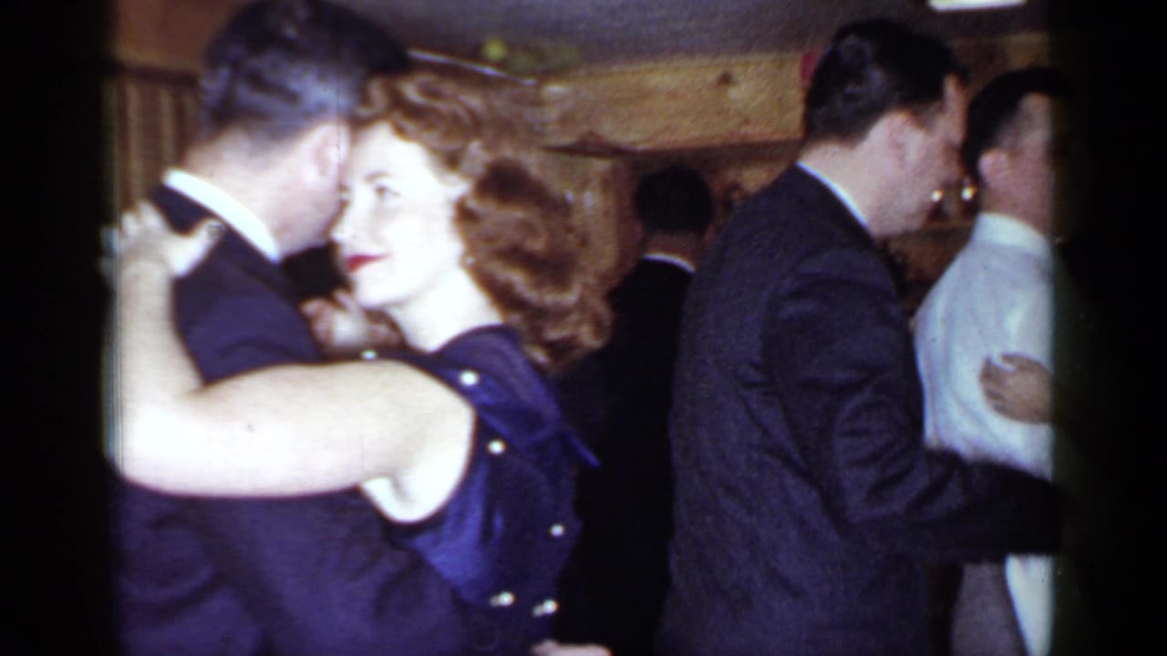 Adults in formal attire dance closely in a wood-paneled bar.