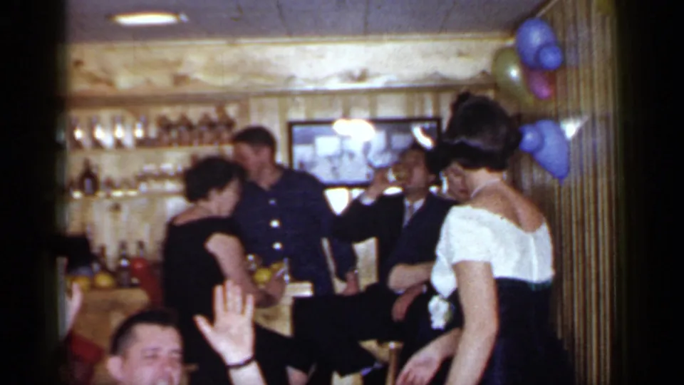 Adults dance and socialize beside a stocked bar and balloons in a 1966 Mineola home-movie party scene.