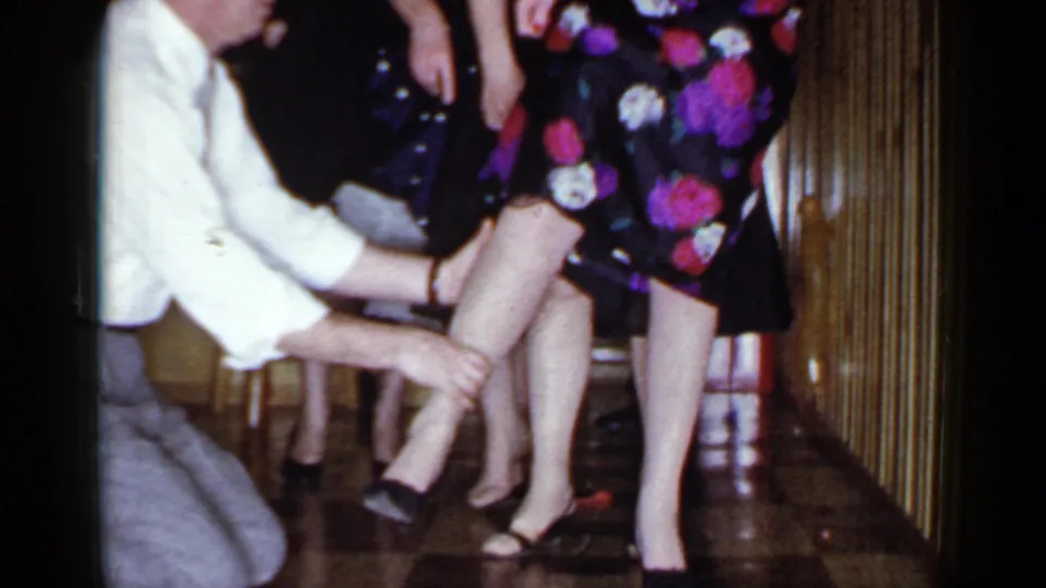 At the end of the clip, the blindfolded man kneels beside a woman in a dark floral dress during the 1966 Mineola party game.