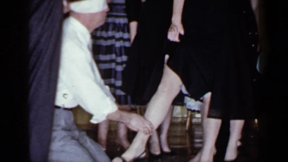 At the end of the 1966 Mineola clip, the blindfolded man kneels before women lined up in dresses indoors.