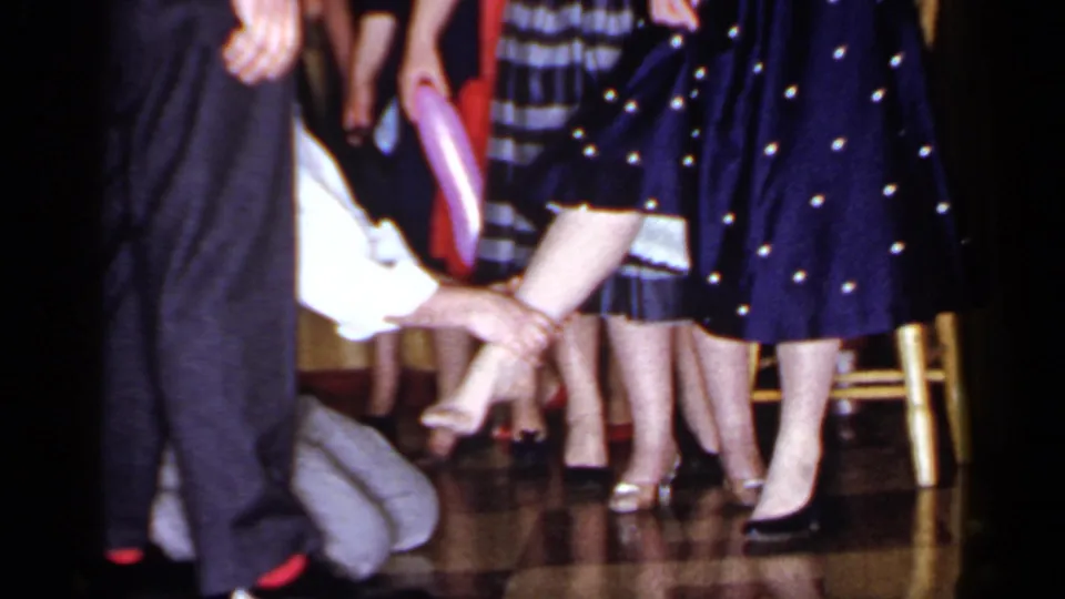 The final frame keeps the focus on the kneeling man and woman's foot, surrounded by adult guests in 1960s party clothing.