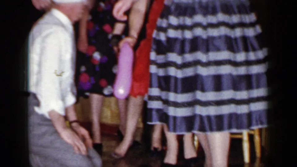 The man remains kneeling near women in red, floral, and striped dresses, with a pink balloon visible in the 1966 Mineola interior scene.