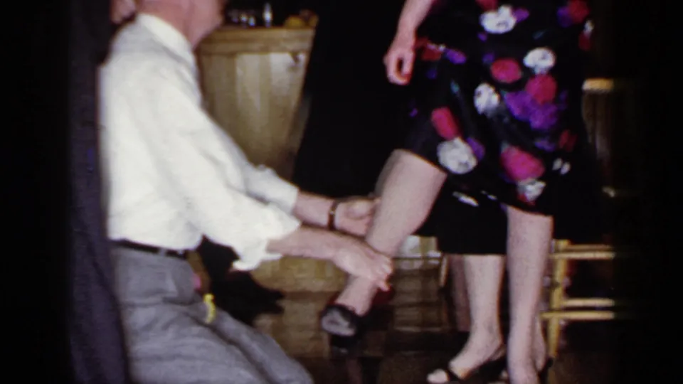In the final Mineola frame, the blindfolded man remains on his knees, holding the woman's leg as adults stand nearby.