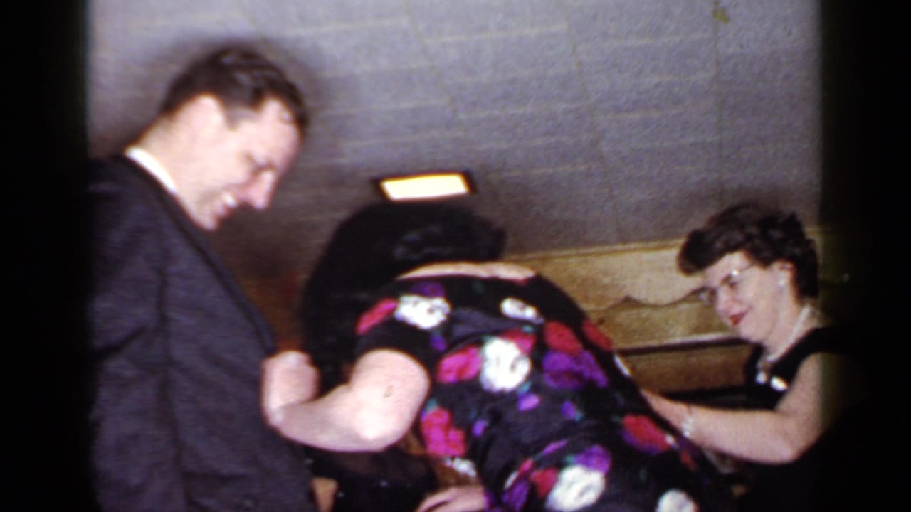 Guests lean together as a blindfolded man sits nearby in a low-ceiling room.