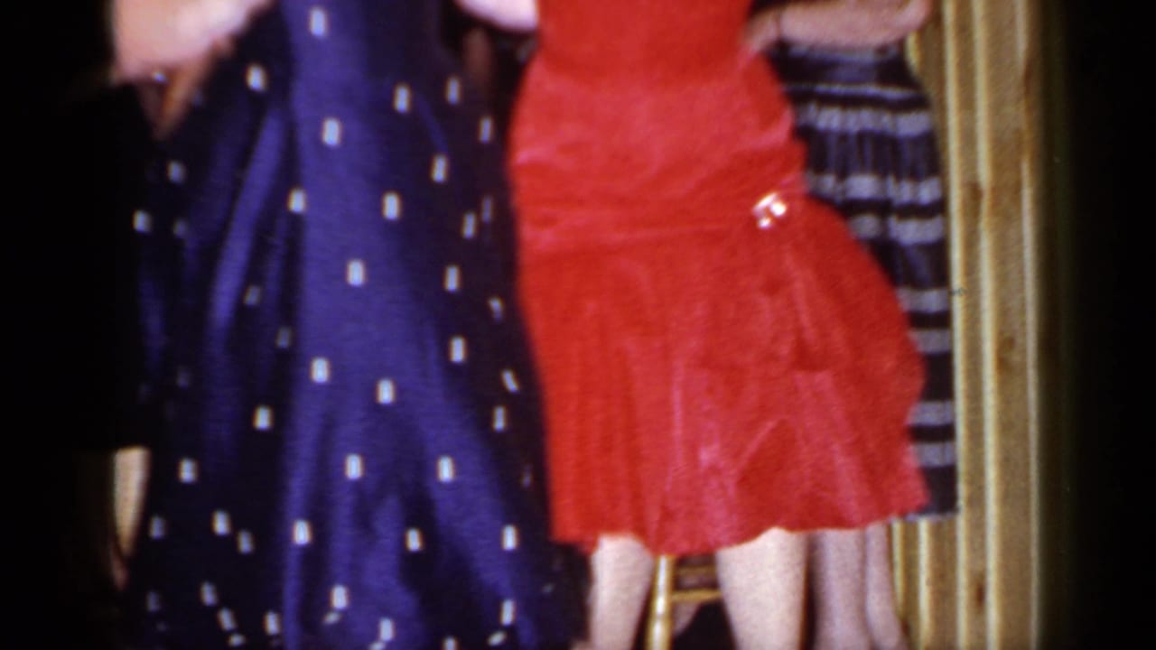 Two women in red and navy dresses dance in front of a dark indoor background.