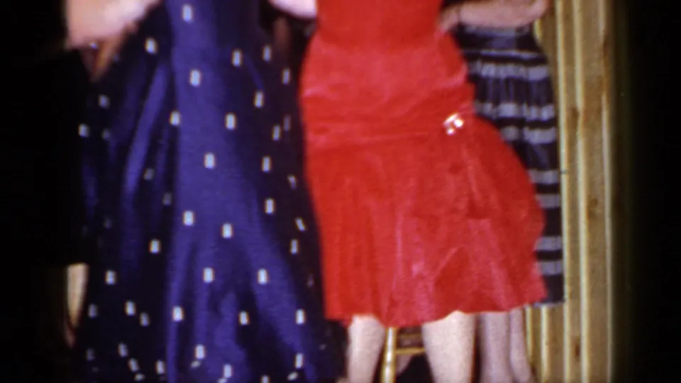1966 Mineola home-movie frame showing two women mid-dance in red and navy polka-dot dresses with motion blur.