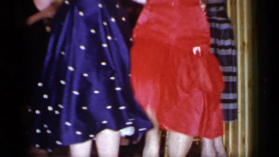 1966 Mineola home-movie still of two women dancing, with red fabric and a navy polka-dot skirt filling the foreground.